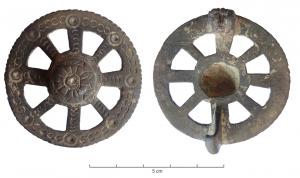 FIB-5144 - Fibule discoïdalebronzeFibule en forme de roue à 8 rayons, le centre du moyeu et les intersections avec la jante sont marqués de cercles oculés, le reste de petites incisions. Au revers, ressort en fer monté sur axe entre deux plaquettes.
