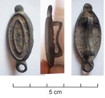 JHA-4042 - Passant de harnaisbronzePassant pourvu au revers d'une bélière rectangulaire. L'applique est de forme ovale, avec un décor champlevé en ovale inscrit; aux extrémités, un bouton d'un côté et un anneau de l'autre.