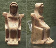 STE-2007 - Statuette : déesse trônantterre cuiteFigurine moulée figurant une déesse assise sur un trône, diadémée et enveloppée dans un long manteau qui recouvre la tête; les pieds sont posés sur un petit tabouret, le bras gauche posé sur la poitrine.