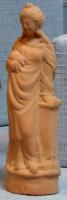 STE-3009 - Statuette : personnage fémininterre cuiteFigurine moulée représentant une femme drapée (chiton et himation), sur un socle cylindrique; la main gauche s'appuie sur une colonne près de la hanche, la main droite tient un nourrisson contre le sein droit.