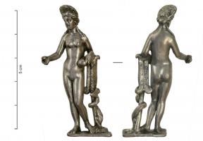 STE-4053 - Statuette : Aphrodite - Vénus appuyée à un tronc d'arbreargentLa déesse nue et diadémée, en appui sur la jambe droite, tend un objet de la main droite (miroir ?), tandis que la gauche tient une boule, sans doute la pomme des Hespérides. Ses longs cheveux retombent sur ses épaules et elle s'appuie à gauche sur un vêtement jeté sur un tronc d'arbre, autour duquel s'enroule un serpent (ou un dauphin ?) ; plaquette de sol.