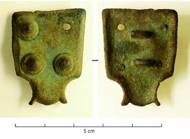 ACE-5034 - Applique de ceinturebronzeTPQ : 550 - TAQ : 750Applique rectangulaire constituée d'une plaque presque carrée, prolongée par une bélière quadrangulaire, et solidement maintenue sur le support en cuir par deux bélières coulées au revers; la face externe porte 4 faux rivets en bossettes.