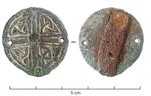 AGR-6020 - Agrafe circulaire
bronze, fer
Médaillon circulaire, à décor géométrique incisé (croix, entrelacs) ; près des bords, quatre petites  perforations dont deux servent à fixer, au revers, une bande de fer rectangulaire certainement liée au mode de fixation.