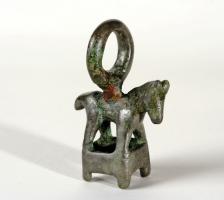 AML-3034 - Amulette : cage surmontée d'un cheval
bronze
Amulette-cage, dont le corps ajouré a pu enserrer une pierre ou un galet, comme sur le type non figuré; l'objet figure un cheval debout, monté sur un cadre quadrangulaire terminé par de petites suuspensions, et surmonté d'un fort anneau.