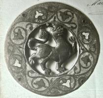 APM-6001 - Applique de coffret
bronze
Applique circulaire, bande externe émaillée à décor de rinceaux végétaux; au centre, motif ajouré dans un cercle : lion, aigle ou autre animal