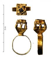 BAG-6004 - Bague à édiculeor, pierreTPQ : 800 - TAQ : 900Bague à jonc plat, dont e chaton s'élargit pour former un édicule de plan carré, à fenêtres géminées sur les côtés, surmonté d'une pierre carrée sur pointe, encadrée de cabochons.