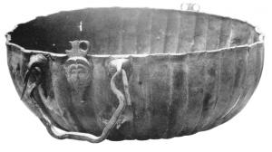 BAS-4004 - Bassin de type Boesterd 196
bronze
Bassin profond, à panse côtelée et à bord oblique, pourvu d'une suspension mobile jouant sur deux attaches fixées par brasure, ainsi que d'une paire d'anses mobiles rattachées à des attaches à figure humaine et doubles anneaux, également fixées par brasure entre les attaches de la suspension.