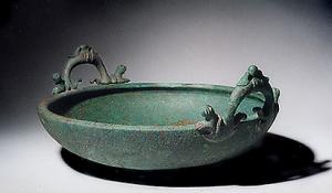 BAS-4013 - Bassin de type Tassinari S.3200
bronze
Bassin à anses à crochets : vasque basse, à bord épaissi et aplati sur le dessus ; les anses de forme sinusoïdale, qui comportent ici un décor végétalisant, remontent de part et d'autre pour prendre appui sur la lèvre.