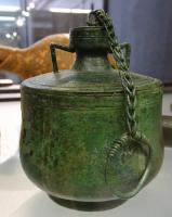 BLS-4124 - Balsamaire
bronze
TPQ : 1 - TAQ : 300
Balsamaire composé de plusieurs parties assemblées par brasure : un corps cylindrique posé sur un pied annuaire, une épaule horizontale (carène marquée) prolongée par un col étranglé et un bord tubulaire, fermé par un bouchon assujetti à une chaînette tressée; deux anses anguleuses, fixées sur e col et sur l'épaule.