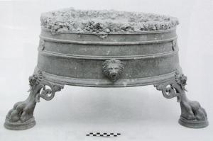 BRS-4002 - Brasero circulaire
bronze, fer
Brasero constitué d'un corps cylindrique, porté par trois supports en forme de patte de fauve, avec des appliques (têtes de lion, de Ménade…) sur la paroi entre les supports; une ceinture de fer équipée de barres parallèles, posée sur la partie en bronze, supportait directement les braises.