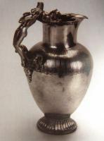 CRU-2001 - Cruche à anse anthropomorphe
argent
Cruche à bec trilobé, col cylindrique, panse ovoïde et piedouche godronné ; l'épaule est également ornée de godrons incisés ; l'anse formée d'une figurine entière, cambrée, est accostée sur la lèvre de deux lions couchés et en bas de deux béliers.