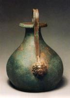 CRU-4016 - Cruche de type Tassinari 5100/5200
bronze
Cruche à panse ovoïde, col étroit de forme conique, lèvre déversée retombant vers l'extérieur sur un bandeau d'oves. L'anse surélevée, en forme de ruban creusé d'une cannelure vers l'extérieur, se termine par une attache en forme de visage largement encadré de mèches de cheveux.