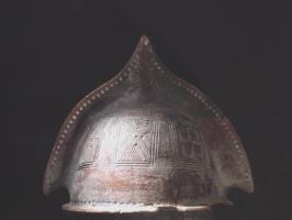 CSQ-1012 - Casque à crête
terre cuite
Imitation en argile d'un casque à crête, reproduisant les deux coques latérales réunies sur un axe du timbre, avec un décor de bossettes.