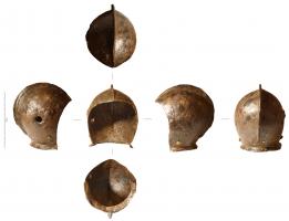 CSQ-8001 - Casque 
fer
Casque enveloppant la tête jusqu'à la nuque avec une crête sagittale d'avant en arrière, un léger rebord en partie basse au niveau du cou. Présence de 2 gros rivets avec leurs bossettes en laiton finement ciselées en bas vers l'avant, pour tenir un possible colletin ou gorgerin et deux autres rivets également en laiton, plus petits, à l'arrière au niveau de la nuque de chaque côté de la crête. Deux autres gros rivets temporaux devaient supporter un mézail en protection pour le visage.