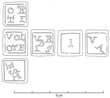DEJ-4005 - Dé inscrit
schiste bitumineux
Dé cubique comportant, au lieu des points habituels, une suite de mots de 1 à 6 lettres, chacun encadré d'un filet : en général,  i / va / est / orti / Caius / volo te  (variantes : urbis / Italia ; croix pattée).