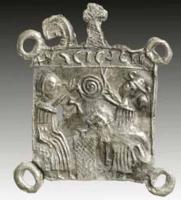 ESP-7020 - Enseigne de pèlerinage : saint Eloi de Noyon
plomb
Plaque carrée surmontée de l'inscription : S.ELIGIVS (ou S. SCI ELIGII, parfois : NOVIOMENSIS) ; elle représente à droite Eloi assis, de face et tenant la crosse d'une main, brandissant de l'autre, au centre de la composition, un