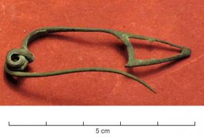 FIB-31016 - Fibule de schéma La Tène III
bronze
TPQ : -75 - TAQ : -50
Fibule reproduisant le schéma La Tène II (arc filiforme très tendu, redressé et rattaché à l'arc par une bague), avec ressort bilatéral à 4 spires et corde interne, mais en construction coulée et donc massive ; bague généralement moulurée en tonnelet ; porte-ardillon triangulaire ou souvent trapézoïdal, fenestré.