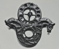 FIB-41268 - Fibule émaillée
bronze
TPQ : 150 - TAQ : 300
Fibule composée d'une couronne émaillée de logettes triangulaires obliques autour d'un vide central, accostée de deux têtes de chevaux divergentes, avec émaux sur l'encolure et crinière incisée; au-dessus, roue de char à quatre rayons, avec moyeu émaillé de même que la jante de la roue.