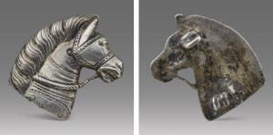 FIB-41769 - Fibule zoomorphe : tête de chevalargentTPQ : 150 - TAQ : 260Tête de cheval harnaché, tournée vers la droite, avec la crinière soigneusement peignée, harnais de tête et rênes ; série de pendants circulaires sur l'épaule ; au revers, ressort monté sur axe sur une, ou parfois deux plaquettes coulées ; porte-ardillon en crochet perpendiculaire à l'aiguille.