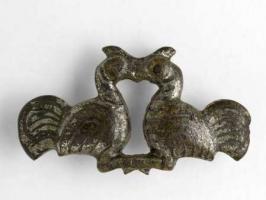 FIB-4290 - Fibule zoomorphe, groupe : combat de coqs
bronze
TPQ : 40 - TAQ : 90
Broche figurant deux gallinacés affrontés, bec et ongles; les corps sont étamés et striés de traits niellés.