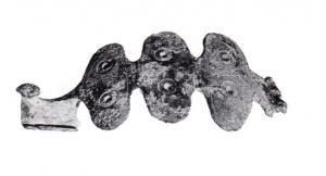 FIB-4642 - Fibule dérivée d'Alésia
bronze
TPQ : -20 - TAQ : 10
Fibule dérivée du type Alésia, c'est-à-dire à arc plat, charnière repliée vers l'intérieur et pied redressé, mais ici terminé par un bouton plat à la place de l'élément transversal du type d'origine ; les contours de l'arc sont ici découpés, formant trois plaques ovales transversales, ornées de cercles oculés ou percées.