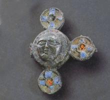 FIB-4696 - Fibule émaillée cruciforme
bronze
TPQ : 150 - TAQ : 300
Fibule de forme non circulaire,  mais de composition rayonnante, sur plan carré : 4 disques émaillés entourent un masque humain stylisé.