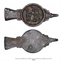 FRT-7021 - Ferret à médaillon figurébronzeTPQ : 1400 - TAQ : 1550Ferret en trois parties : l'attache supérieure rivetée sur l'extrémité de la ceinture, avec un décor gravé; une partie médiane en forme de médaillon ajouré, orné d'un relief figuré : femme tenant un enfant à gauche, et chevalier avec lance à droite (ou saint Joseph avec une scie ou un bâton : Sainte Famille...?); un lest en forme de tête animale.