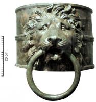 GGV-4001 - Garniture de gouvernail
bronze
Embout de gouvernail formé d'un cylindre de tôle épaisse (ép. > 10 mm) renforcé par des nervures aux extrémités et au centre ; décor en applique : tête de lion tenant un gros anneau de bronze dans sa gueule.