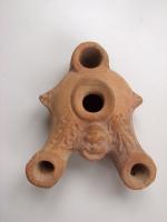 LMP-3128 - Lampe à deux becs
terre cuite
TPQ : -120 - TAQ : -50
Lampe à deux becs allongés,à la partie supérieure décorée d’une palmette, et large trou de mèche ou de remplissage, arrondi, à l’arrière. Sur l’épaule, deux petits tenons triangulaires latéraux, placés diamétralement. Entre les becs, petit masque grimaçant. Large trou de remplissage central entouré d’un cercle en relief.Base plate définie par un cercle incisé.