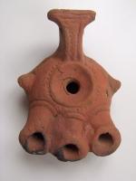 LMP-3129 - Lampe orientale 3 becs : Alpha
terre cuite
TPQ : -120 - TAQ : -50
Lampe à réservoir rond avec ailerons latéraux. Trois longs becs tubulaires accostés. Anse avec petit réflecteur en forme de T. Argile orange, engobe perdue. Base plate. Marque : Alpha incisé.