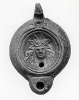 LMP-41318 - Lampe Loeschcke VIII Tête dionysiaque
terre cuite
TPQ : 90 - TAQ : 150
Lampe à bec court défini par un trait horizontal. Médaillon décoré d'une tête dionysiaque avec riche parure végétale sur le front.