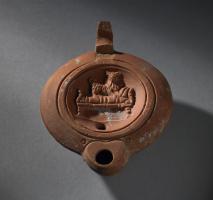 LMP-41326 - Lampe Loeschcke VIII Chien
terre cuite
TPQ : 90 - TAQ : 150
Lampe à bec court cordiforme. Médaillon décoré d'un chien sur un lit (Sothis?).