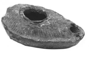 LMP-41495 - Lampe pantoufle byzantine 
terre cuite
TPQ : 400 - TAQ : 600
Lampe allongée à bec incorporé, épaule décorée de traits rayonnants en relief. Base ovale ornée d'une feuille de palme et d'une inscription grecque en relief.