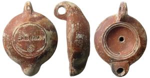 LMP-41565 - Lampe à bec rond limité par un trait : GABINIA
terre cuite
TPQ : 80 - TAQ : 140
Lampe moulée, anse verticale percée à deux sillons sur la tranche. Réservoir circulaire à profil biconvexe. Bandeau penché vers l'extérieur,. disque en cuvette limitée par deux sillons concentriques. Trou d'évent. Bec arrondi limité par un trait droit. Base circulaire plate en léger relief limitée par un sillon. Estampée GABINIA  surmontant deux petits cercles concentriques en creux.  Engobe rouge marron sur toute la lampe.