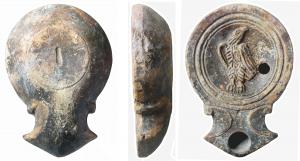 LMP-41588 - Lampe à bec triangulaire : Aigle, planta pedis
terre cuite
TPQ : 50 - TAQ : 100
Lampe moulée, sans anse. Réservoir circulaire à profil convexe. Bandeau étroit et plat. Disque en cuvette limitée par trois sillons concentriques. Décor : aigle à la tête levée. Large bec triangulaire à deux volutes simples se poursuivant sous la lampe. Base circulaire plate en léger relief limitée par un sillon ; porte une planta pedis en creux. Engobe gris marron sur toute la lampe.