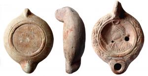 LMP-41798 - Lampe à bec cordiforme : Buste de Séléné / Luna
terre cuite
TPQ : 225 - TAQ : 250
Moulée, anse verticale pleine à deux sillons sur la tranche. Réservoir circulaire à profil biconvexe. Bandeau penché vers l'extérieur au décor de guirlande de laurier noué. Disque en simple cuvette limitée par deux sillons ; sceptre (?) et  buste de Séléné /  Luna à gauche.  Bec arrondi cordiforme au dessous strié. Base circulaire plate en léger relief limitée par un bourrelet souligné par deux sillons. Porte un sigle illisible. Restes d'engobe rouge sur toute la lampe.