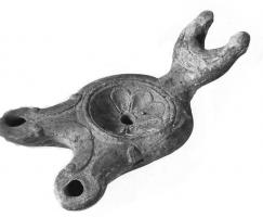 LMP-4210 - Lampe Loeschcke III à deux becs : rosette
terre cuite
TPQ : 80 - TAQ : 150
Lampe de Type Loeschcke IV à deux becs en ogive à volutes  ; disque décoré d'une rosette, anse plastique en forme de croissant de lune.