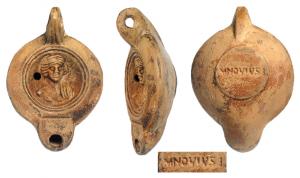 LMP-42131 - Lampe à bec rond limité par un trait : Buste, M NOV IVSTI
terre cuite
TPQ : 120 - TAQ : 180
Lampe moulée, anse verticale percée à deux sillons sur la tranche, circulaire à profil biconvexe. Bandeau lisse penché vers l'extérieur, disque en cuvette limitée par deux sillons concentriques. Décor : buste de femme (ou d'Apollon), coiffure en deux larges bandeaux sur les côtés. Bec arrondi limité par un trait droit ponctué aux extrémités. Base circulaire plate en léger relief limitée par un sillon, estampillée MNOVIVS(t)I. Engobe orangé rouge sur toute la lampe