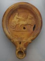 LMP-42301 - Lampe Loeschcke IV : Char
terre cuite
TPQ : 25 - TAQ : 75
Lampe moulée, sans anse; double long bec en ogive encadré de volutes. Médaillon orné d'un char de course à droite, tiré par un bige.