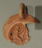 LMP-42400 - Lampe : Apollon citharède 
terre cuite
TPQ : 120 - TAQ : 180
Lampe à bec rond (?). Décor du médaillon : Apollon citharède, assis  de profil à droite sur un rocher, le torse nu, la jambe droite couverte d'une draperie ; à droite, devant le musicien, un animal (chien ?) assis.