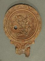 LMP-42401 - Lampe Loeschcke IV : trophée marin
terre cuite
TPQ : 40 - TAQ : 100
Décor du médaillon : trophée marin comprenant au moins un dauphin enroulé verticalement autour d'un gouvernail, un trident dressé et une conque ; autre sujet indéterminé : murène ?