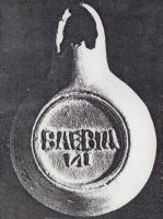 LMP-42417 - Lampe de firme : BAEBIANI
terre cuite
TPQ : 50 - TAQ : 200
Lampe moulée, sans anse. Réservoir circulaire de profil biconvexe asymétrique. Bandeau penché vers l'extérieur porte trois tenons rectangulaires rainurés, non percés, disposés en triangle. Disque en cuvette profonde bordée par un bourrelet qui se poursuite sur le bec le long d'un étroit canal et entoure le méplat. Trou d'évent dans le canal. Base circulaire plate en creux limitée par deux anneaux concentriques enfermant la marque BAEBIANI.