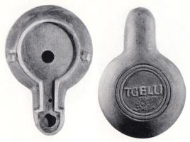 LMP-42435 - Lampe de firme : T.GELLI
terre cuite
TPQ : 100 - TAQ : 200
Lampe moulée sans anse: le réservoir circulaire est de profil biconvexe asymétrique; bandeau penché vers l'extérieur portant deux tenons rectangulaires non percés, sur l'axe horizontal. Disque en cuvette profonde bordée par un bourrelet continu. Bec long au petit canal non communiquant avec le disque, chanfeiné sur les côtés. Base circulaire plate en creux limitée par deux anneaux concentriques enfermant l'estampille moulée T.GELLI, en relief. Engobe rouge brique peu adhérent.