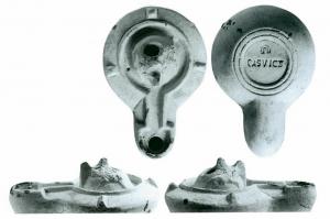 LMP-42513 - Lampe de firme : CASVICT
terre cuite
TPQ : 100 - TAQ : 200
Lampe moulée ; le médaillon circulaire est presque entièrement occupé par une anse plastique hémisphérique, à languette verticale perforée, avec un lion à gauche et un sanglier à droite ; bandeau penché vers l'extérieur portant trois tenons. Le disque communique par un canal ouvert avec le bec, le tout enserré dans un bourrelet Base circulaire plate en creux limitée par deux anneaux concentriques enfermant l'estampille en creux CASVICT, surmontée d'une ove également imprimée.