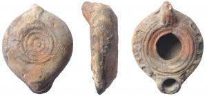 LMP-4589 - Lampe moulée
terre cuite
TPQ : 350 - TAQ : 400
Anse pleine à deux sillons. Réservoir circulaire de profil biconvexe. Bandeau orné d'éléments décoratifs estampés. Petit bec au bout arrondi.  Bourrelets concentriques sur le disque autour d'un grand trou d'alimentation et sur la base.