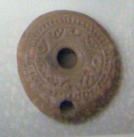 LMP-5006 - Lampe byzantine en galetterre cuiteTPQ : 400 - TAQ : 700Lampe moulée, réservoir circulaire très aplati. Bec percé sur le rebord, flanqué par deux cercles en creux ; traces d'utilisation.  Bandeau orné de deux cercles concentriques enfermant une couronne de points en creux. Le disque porte huit ou neuf demi cercles au décor de points. Un anneau entoure le trou d'alimentation. Base circulaire ornée d'un motif rayonnant ou d'un oiseau. Deux sillons verticaux partent des bords de la lampe et rejoignent la base. Le tout est entouré par une ligne de points.