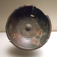 PAT-5003 - Patère
bronze
Patère à bord ourlé vers l'extérieur, orné d'une frise d'oves estampés ; ombilic central, à décor rayonnant incisé, entouré d'une inscription; profil très ouvert posé sur un fond annulaire légèrement tronconique ; manche ?