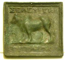 PDS-3003 - Poids grec : Séleucie de PiériebronzePlaque carrée coulée, avec un relief sur la face supérieur : bœuf marchant à aguche (trait de sol), encadré de deux inscriptions : au-dessus, [[SELEYKION]]; au-dessous, [[TETA...]].