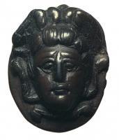 PDT-4010 - Pendentif : tête de Méduse
jais
Pendant ovale ou plus rarement circulaire, figurant une tête de Méduse de face, sans encadrement, le visage aux traits écarquillés encadrés de mèches ondulées, et surmonté de deux ailettes; perforations transversale dans la partie sommitale; revers lisse.