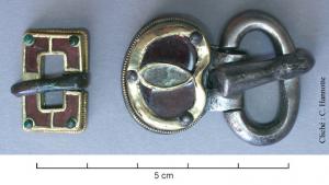 PLB-5605 - Plaque-boucle articuléeargentTPQ : 450 - TAQ : 510Plaque en forme de boîtier réniforme, avec une bordure dont le prolongement ds extrémités s'entrecroise pour délimiter trois champs incrustés de pierres semi-précieuses; anneau également réniforme, de section massive, avec un ardillon épais, section en bâtière.